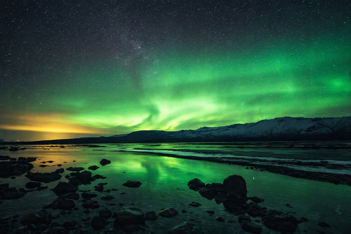 Tromsø Northern Lights scene taken during a Tromso Norway Tours polar night tour, showing powerful green aurora mirrored in the Arctic shoreline and frozen water